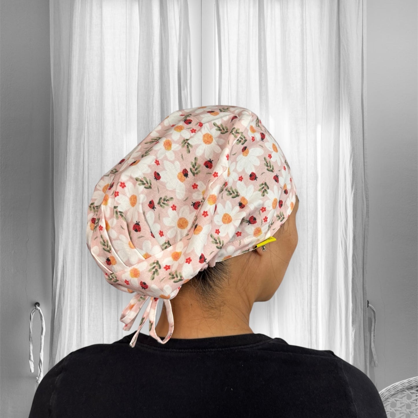 A person wearing a floral-patterned scrub cap. The cap features a design of white flowers with yellow centers and small red accents.
