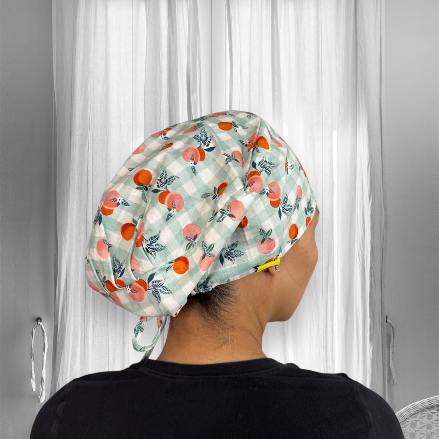 A person wearing a checkered cap with a pattern of oranges and leaves. The cap features pastel green and peach tones.