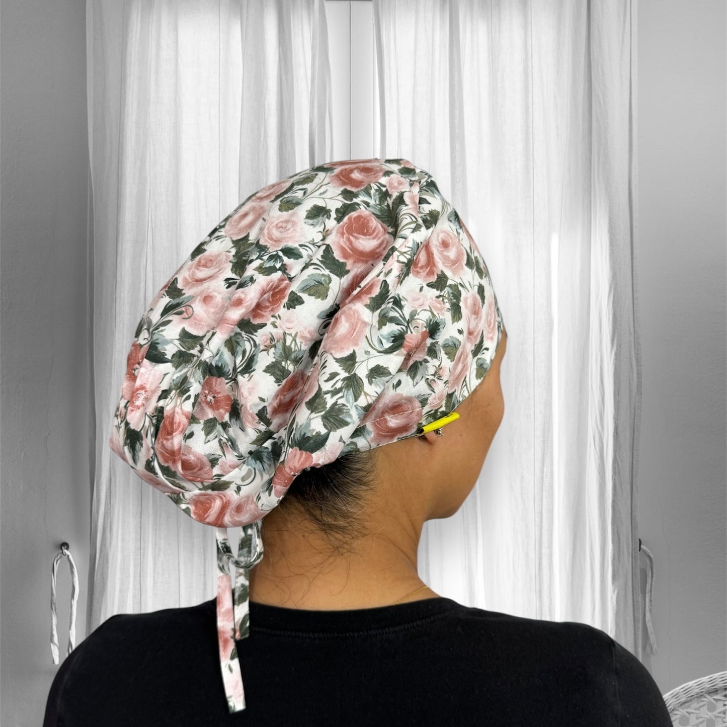 A floral-patterned scrub cap with pink roses and green leaves on a white background.