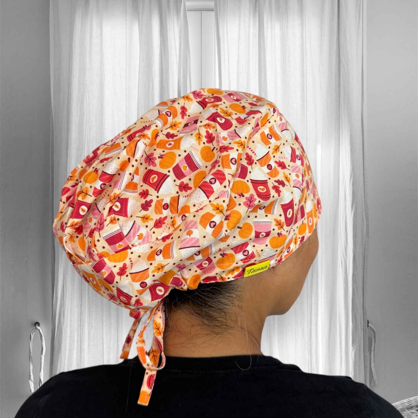 A brightly patterned scrub cap with a vibrant design featuring autumn-themed elements such as leaves and abstract shapes in shades of orange, red, and cream.