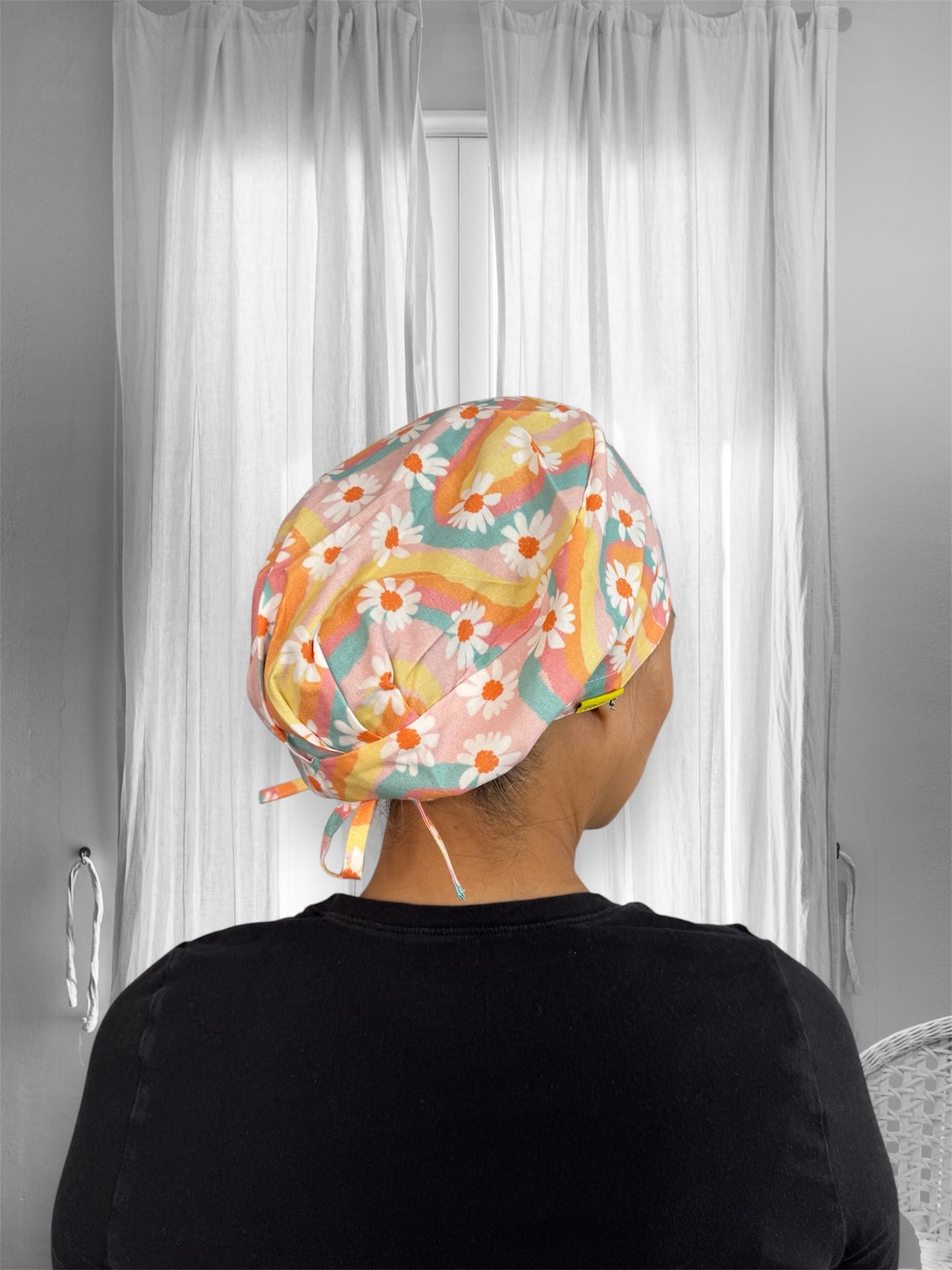 A person wearing a colorful scrub cap with a vibrant pattern of daisies and wavy lines in shades of pink, yellow, orange, and blue.