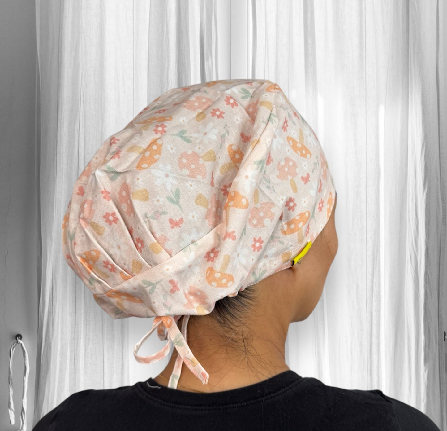 A person is wearing a scrub cap with a light pastel-colored pattern featuring mushrooms, flowers, and leaves.