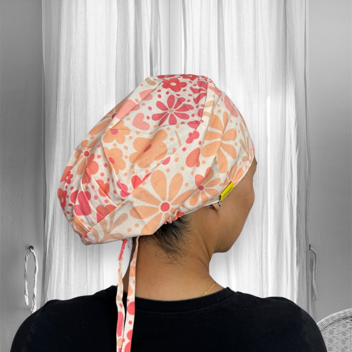 A person wearing a floral-patterned scrub cap, showcasing an array of peach and coral-colored flowers and hearts.