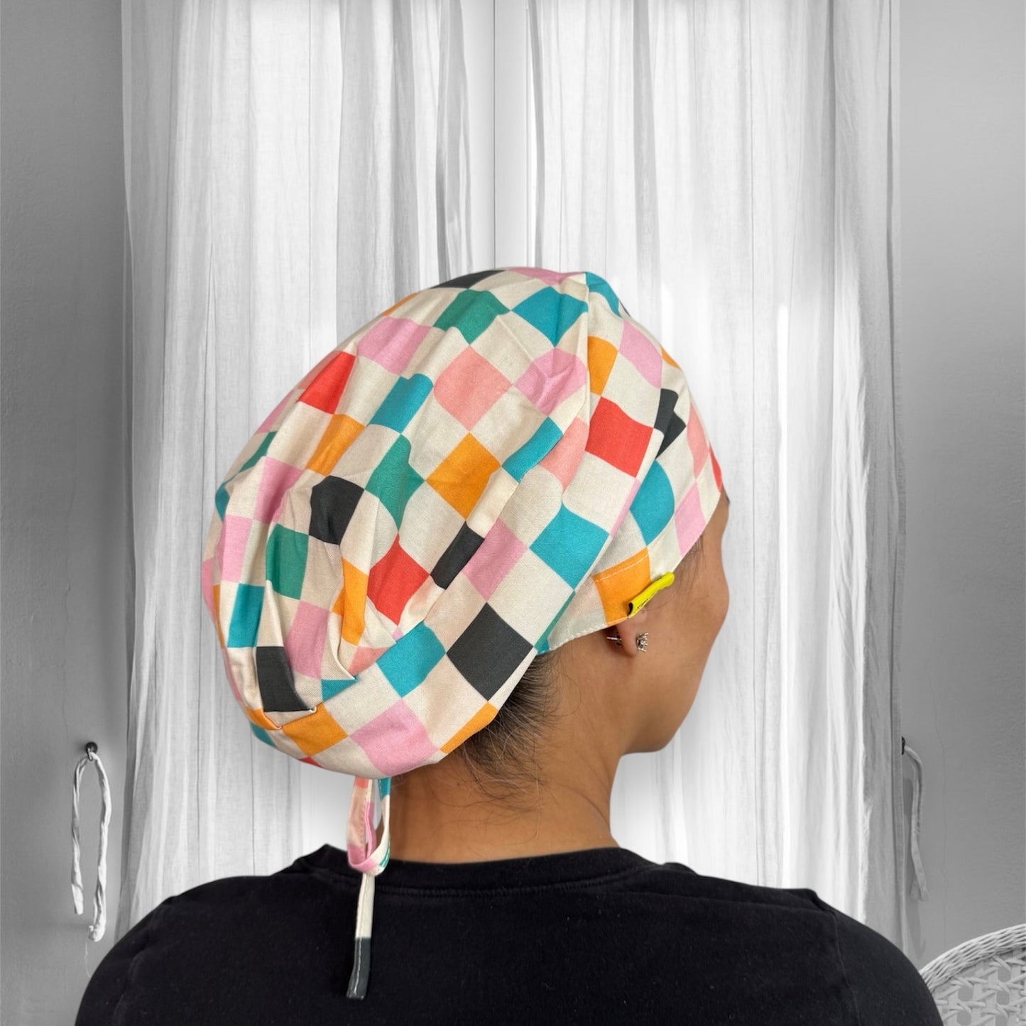 A colorful scrub cap made of fabric featuring a checkered pattern with vibrant colors such as pink, orange, blue, black, and white.