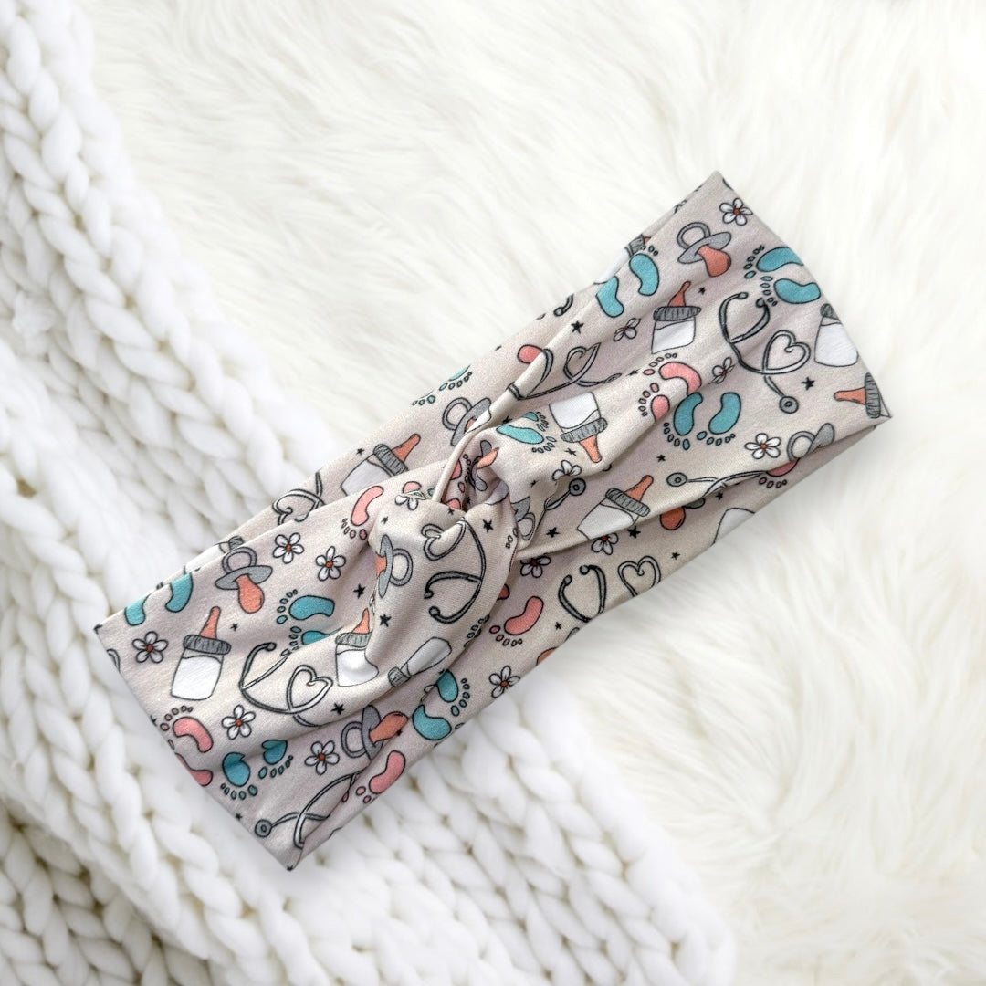 A cute headband featuring a playful pattern of baby accessories like pacifiers, bottles, and tiny footprints in pastel colors.