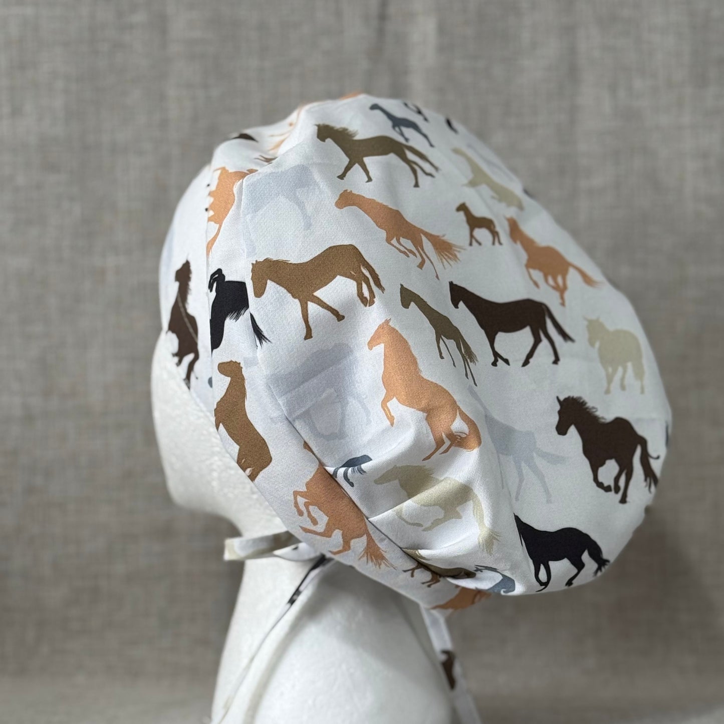 A scrub cap featuring a pattern of various horse silhouettes in shades of brown, black, and grey.