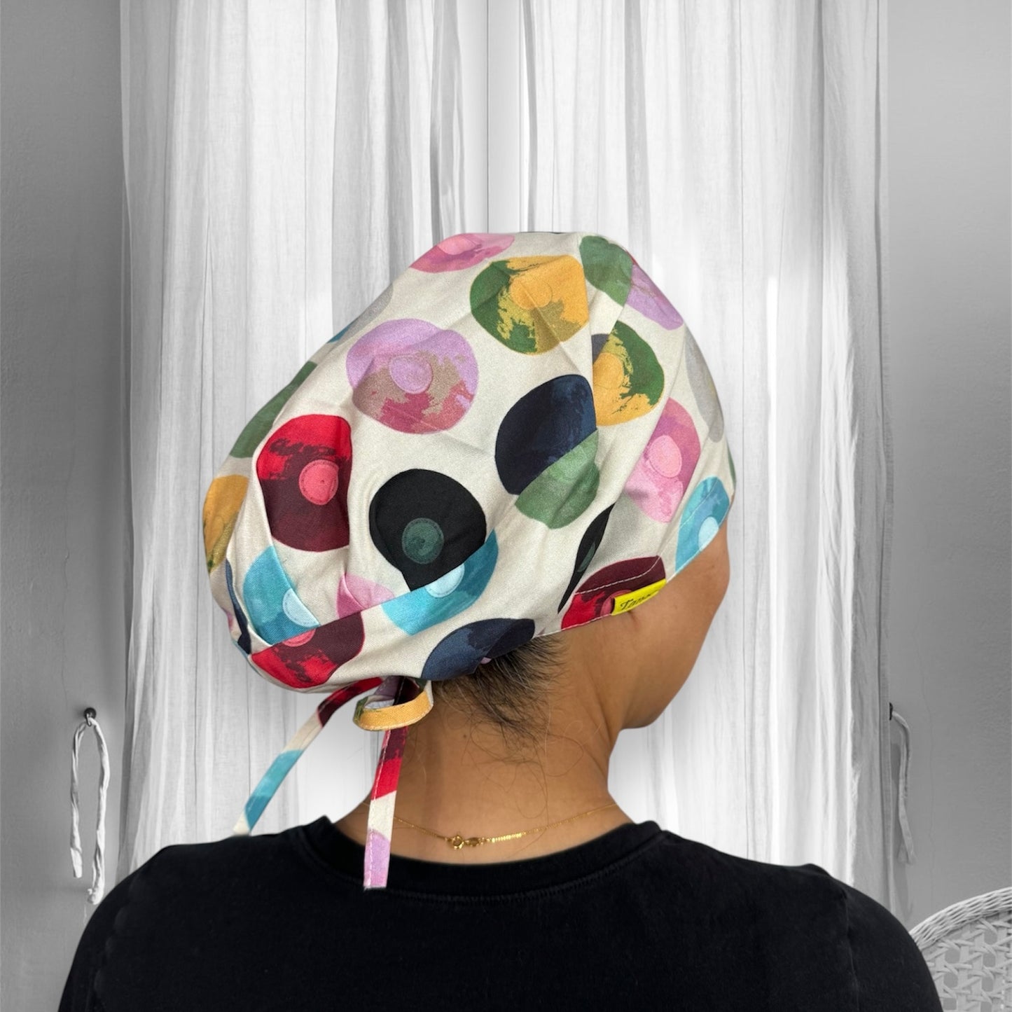 A person wearing a colorful scrub cap featuring various circular patterns in different shades, including red, green, blue, yellow, and black.