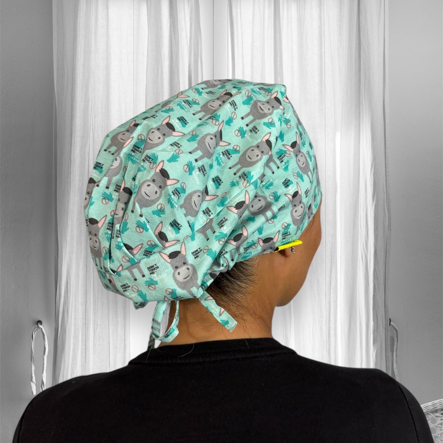 A person wearing a colorful scrub cap featuring a playful donkey pattern. The fabric is light blue with printed cartoon donkeys.