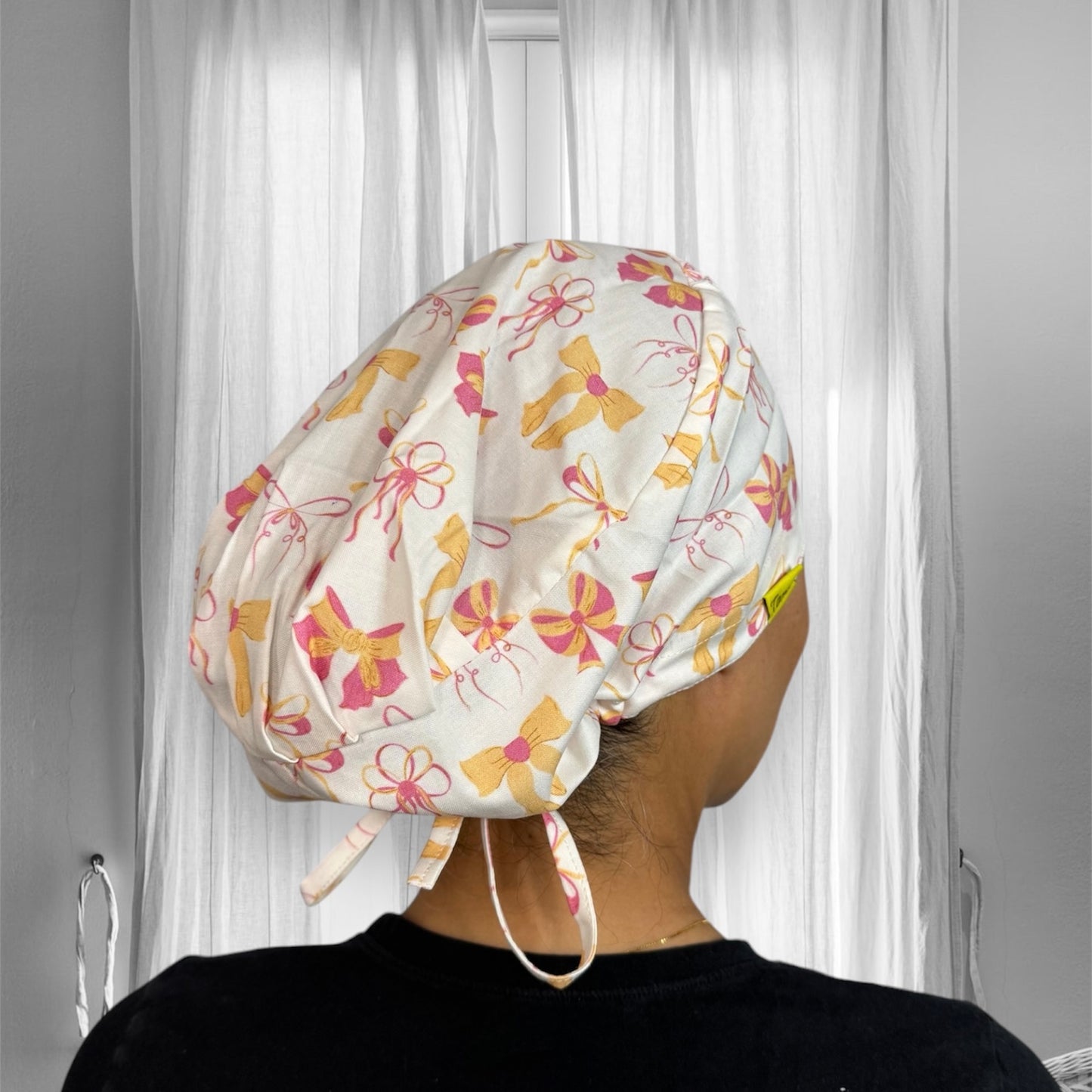 A person wearing a scrub cap with a colorful pattern of bows and flowers in pink and yellow hues.