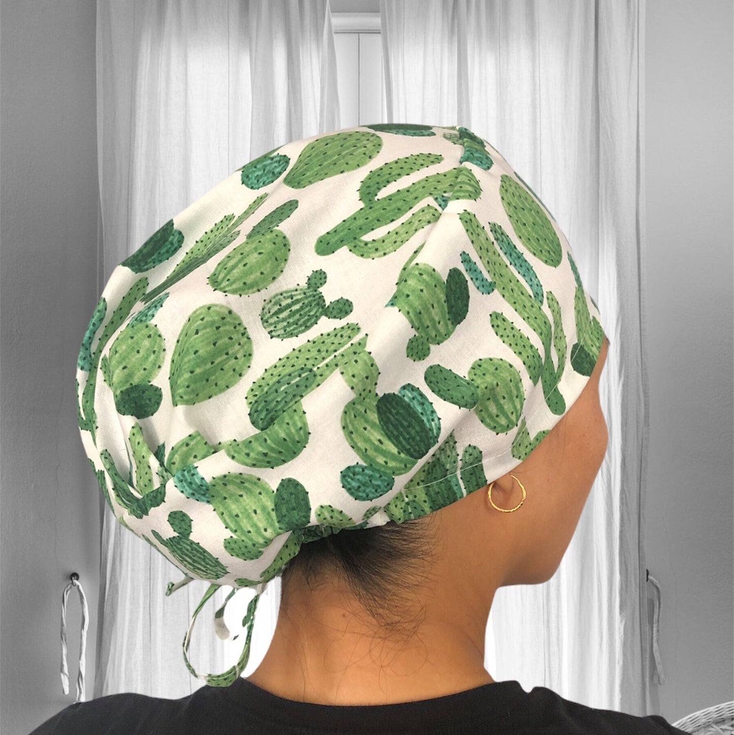 A person wearing a scrub cap with a vibrant green cactus pattern. The cap's design features a variety of cactus species in differing shades of green.