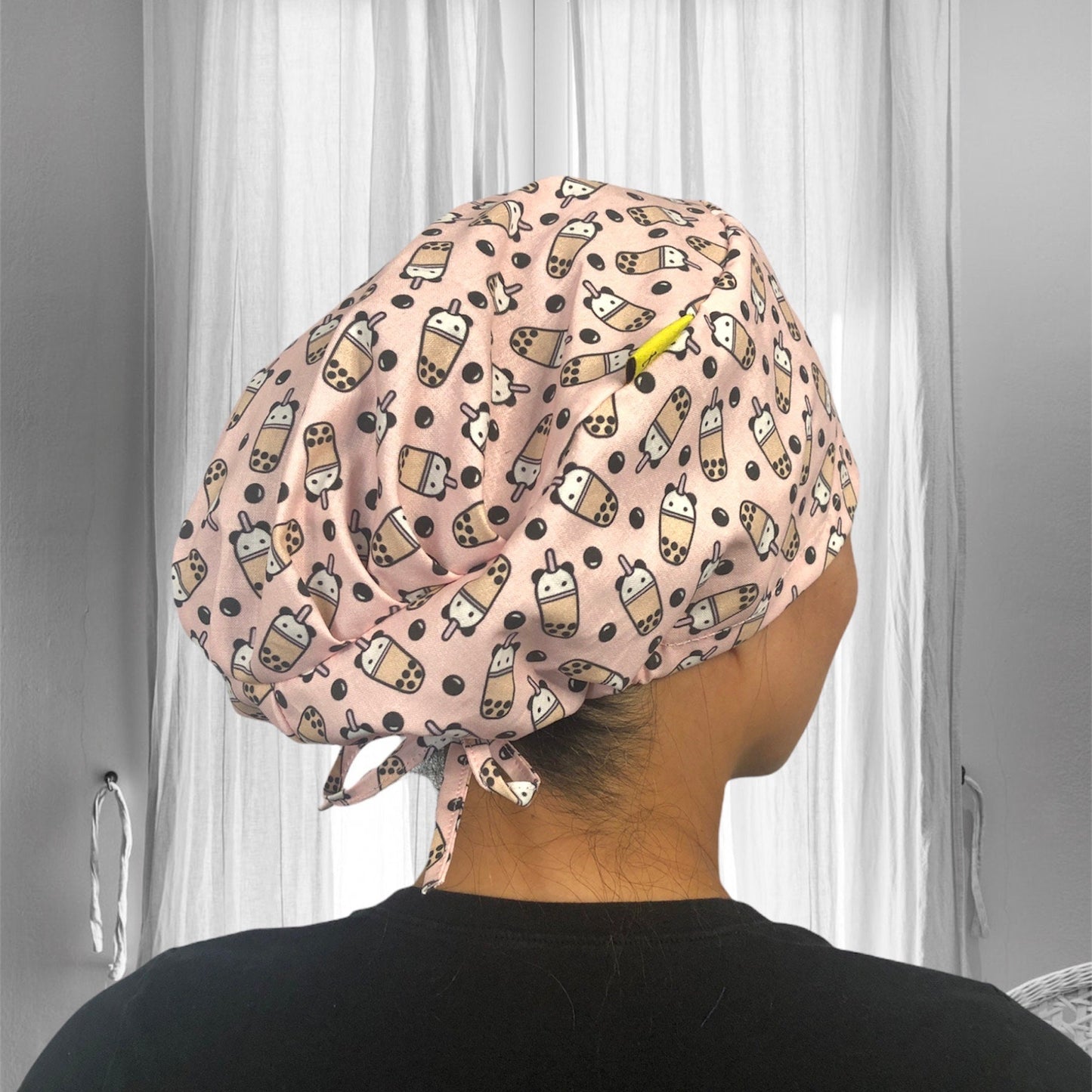 A beige fabric scrub cap featuring a playful pattern with cartoon bubble tea cups and black tapioca pearls.