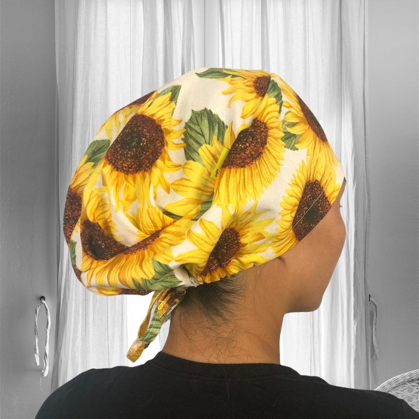 A person wearing a sunflower-patterned scrub cap, with bright yellow sunflowers and green leaves against a light background.