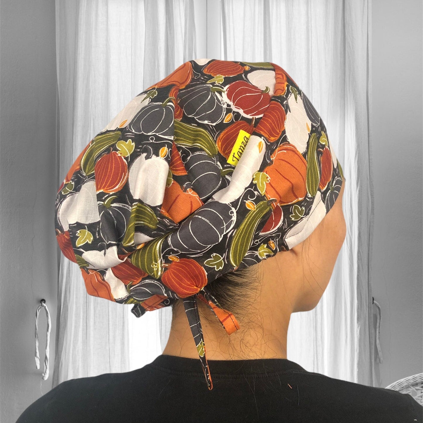 A person wearing a colorful scrub cap featuring a pumpkin and gourd pattern. The cap is styled in autumn colors with shades of orange, green, and white.