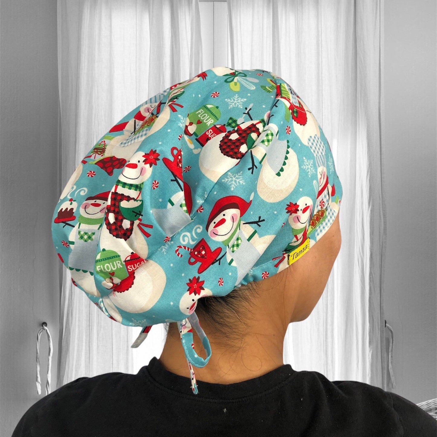 A festive scrub cap featuring cheerful snowmen in winter attire against a light blue background, adorned with snowflakes and holiday motifs.