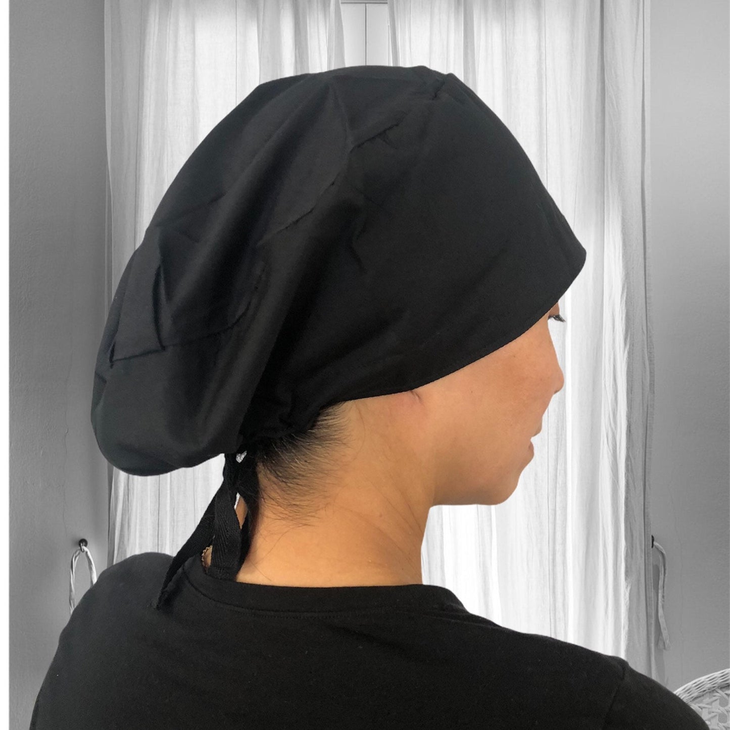 A black scrub cap, viewed from the side, with a tie at the back.