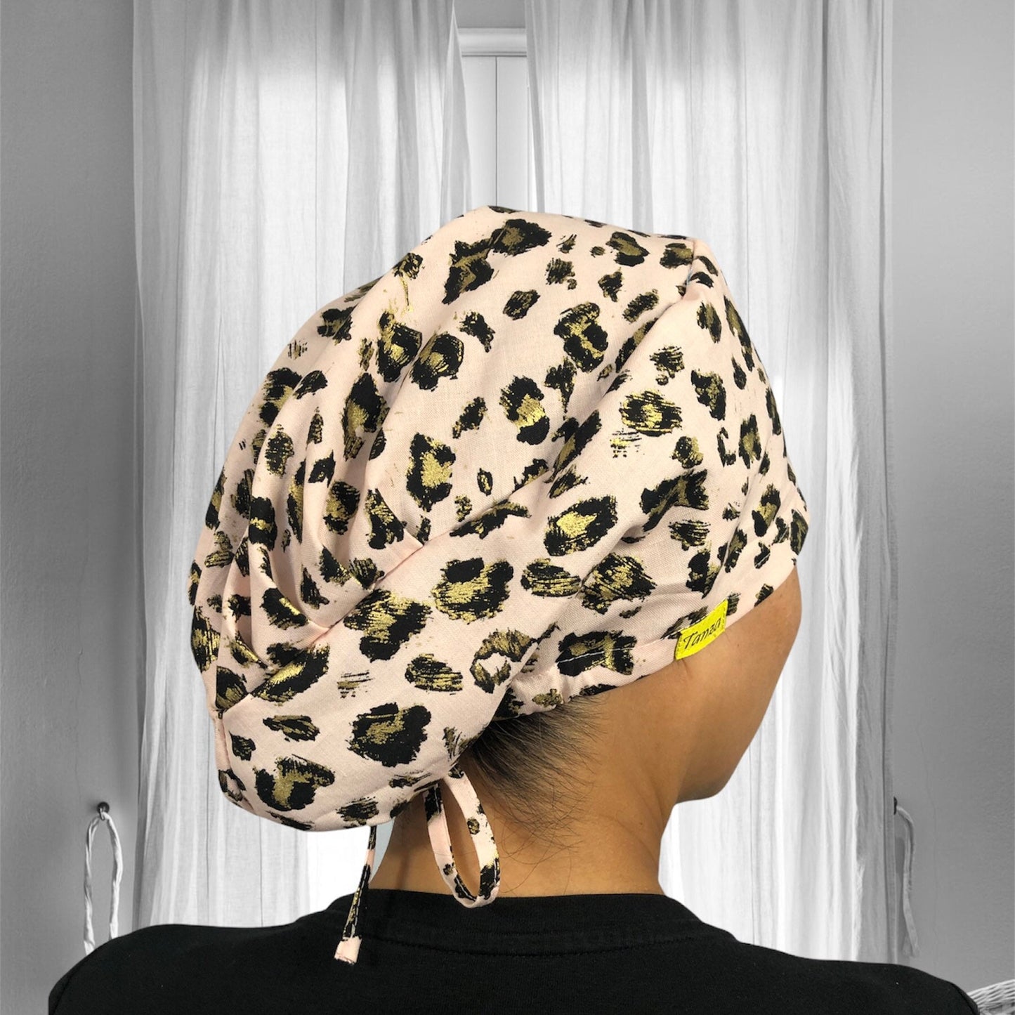 A person is wearing a scrub cap with a beige base and black and gold leopard print design.