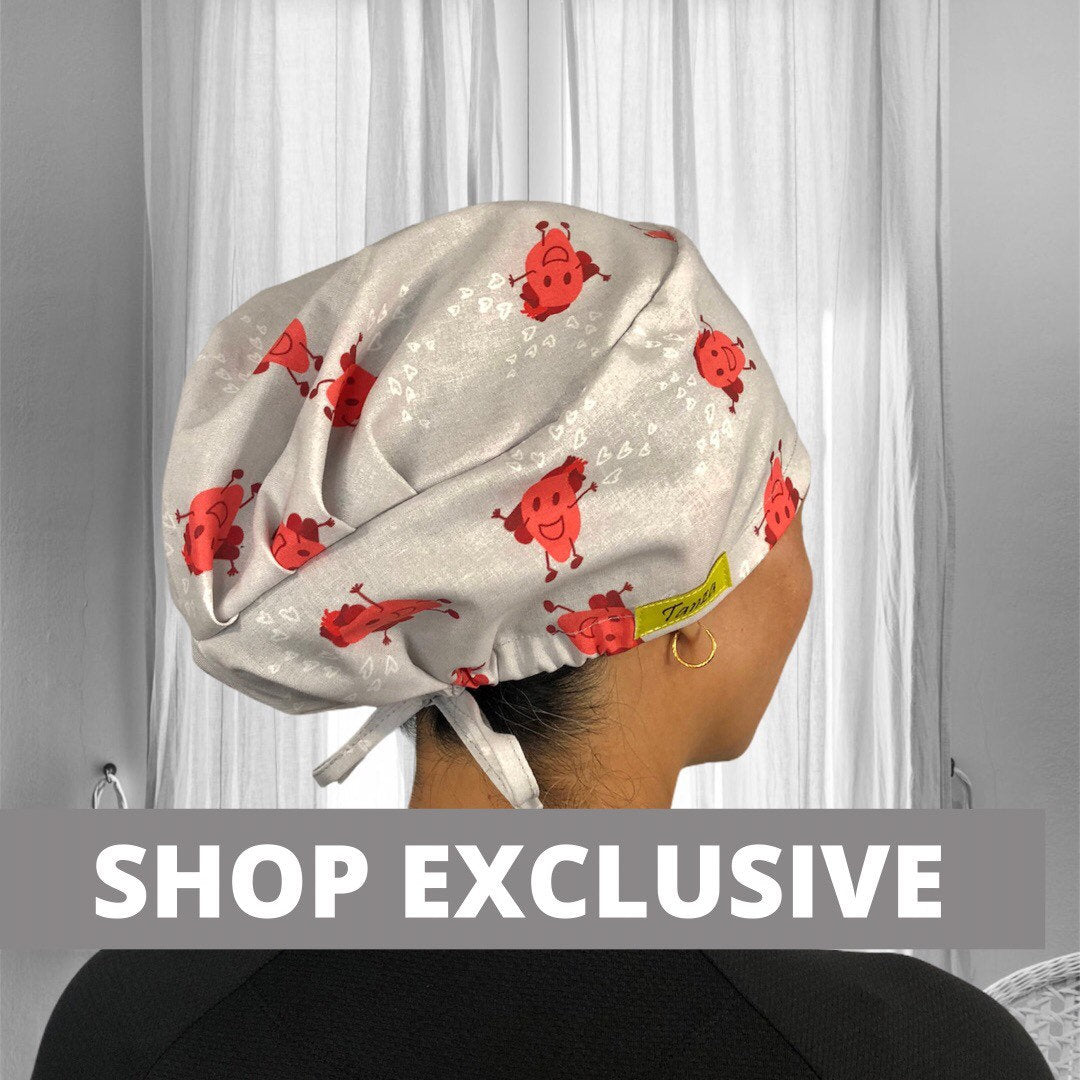 A light grey scrub cap adorned with cheerful red heart characters. The cap features small white hearts scattered around the design. It is secured at the back with a tie.
