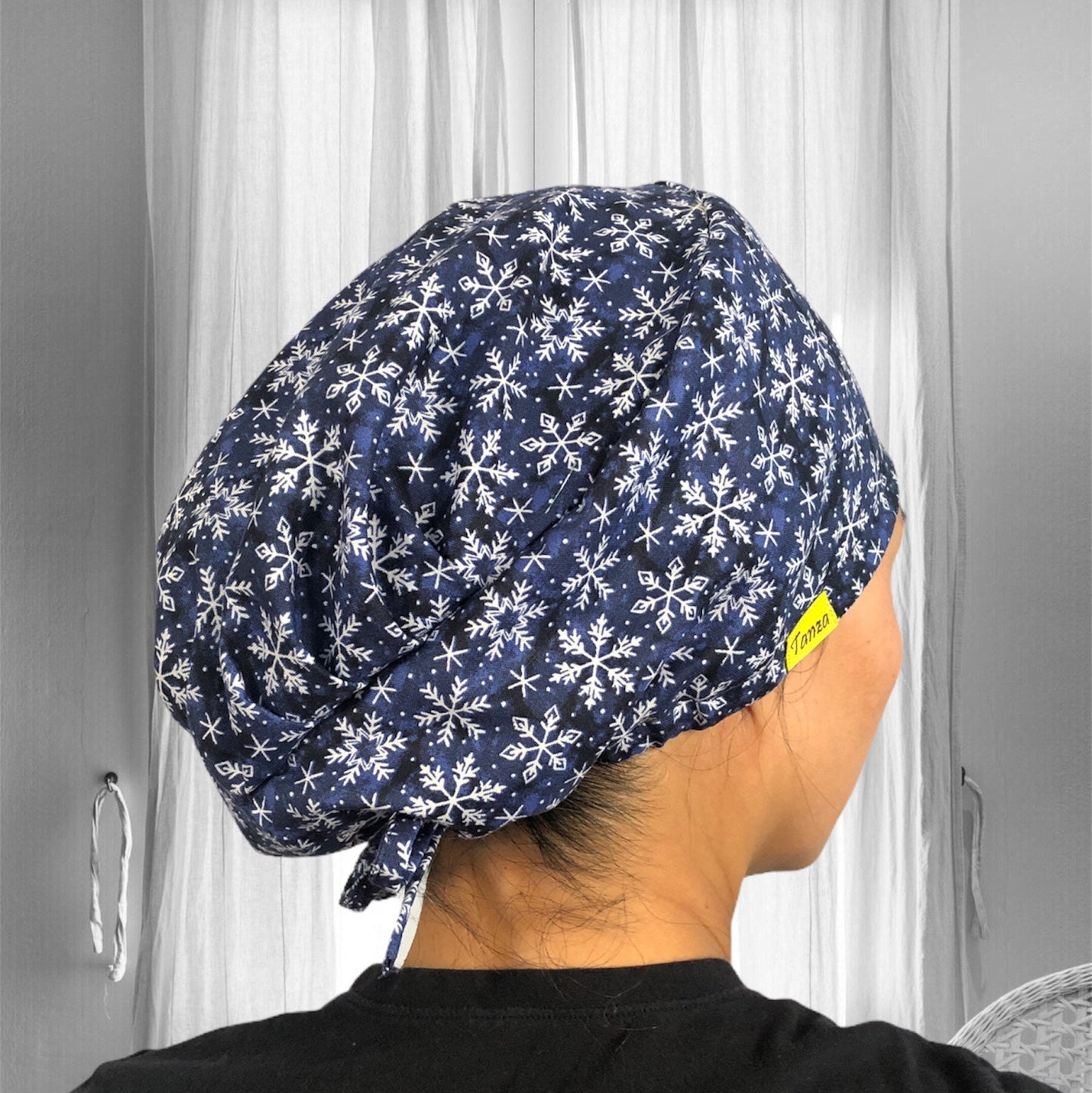 A person is wearing a dark blue scrub cap adorned with a pattern of white snowflakes.