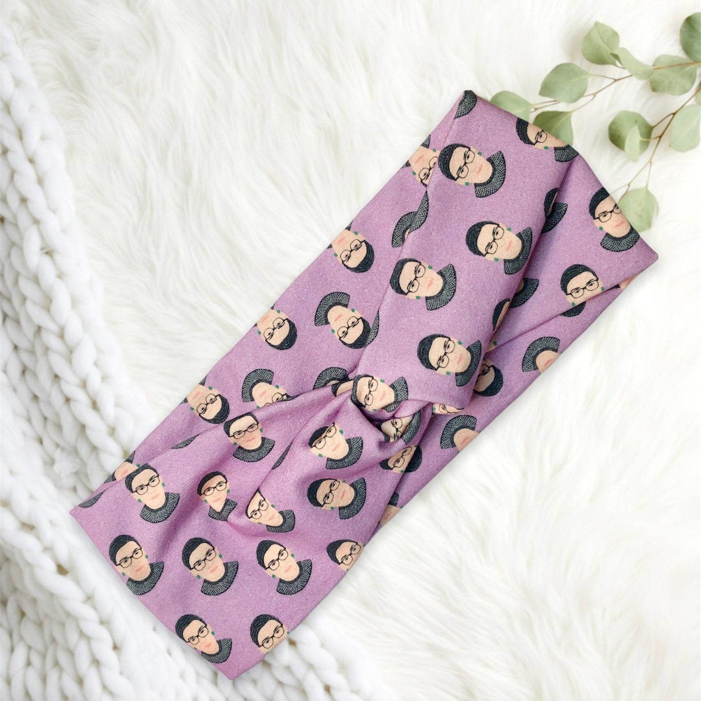 A stylish headband featuring a purple fabric adorned with a repeated pattern of illustrated faces wearing glasses and a distinctive hairstyle.