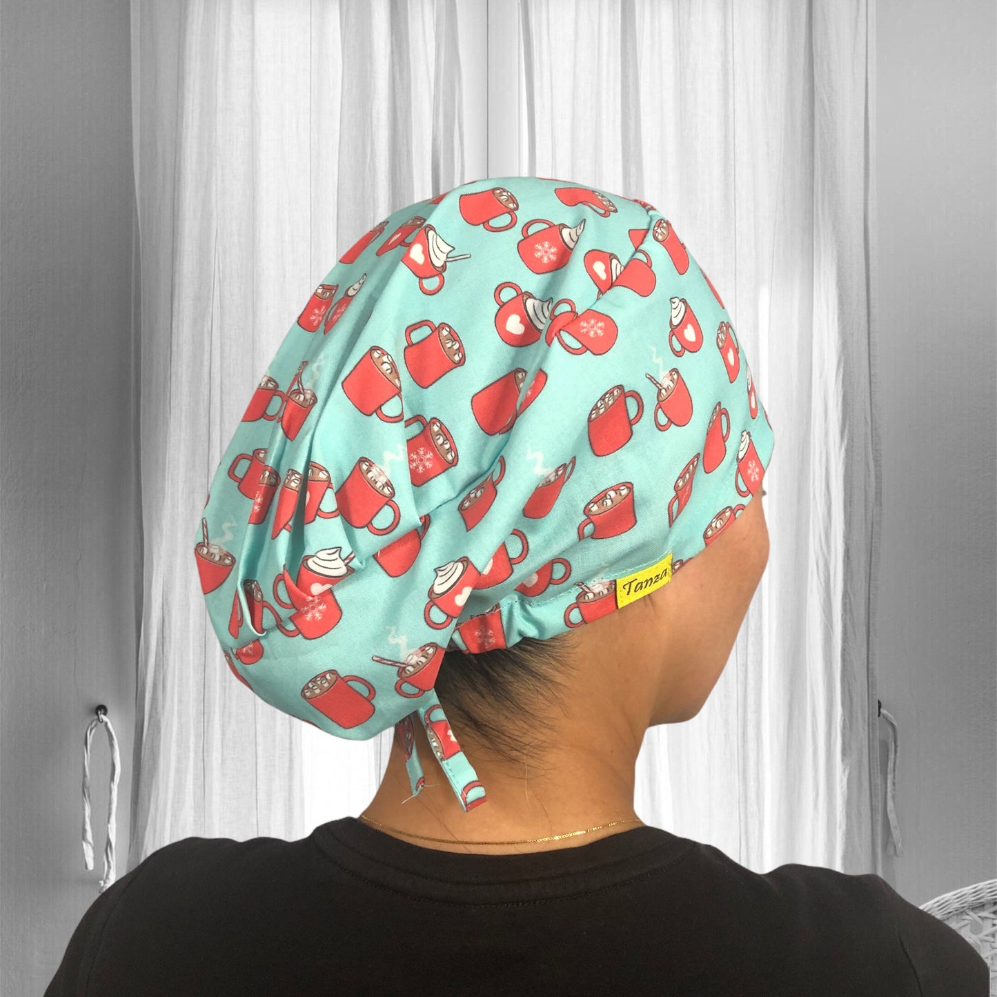 A person wearing a light blue scrub cap adorned with a playful pattern of red mugs filled with whipped cream and steaming hot beverage.