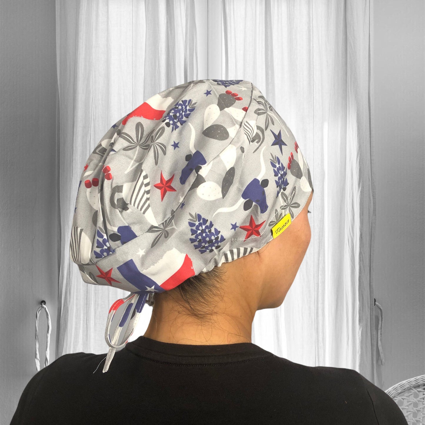 A person is wearing a scrub cap with a pattern featuring stars, stripes, and various abstract shapes. The cap is predominantly grey, with accents of red, white, and blue.