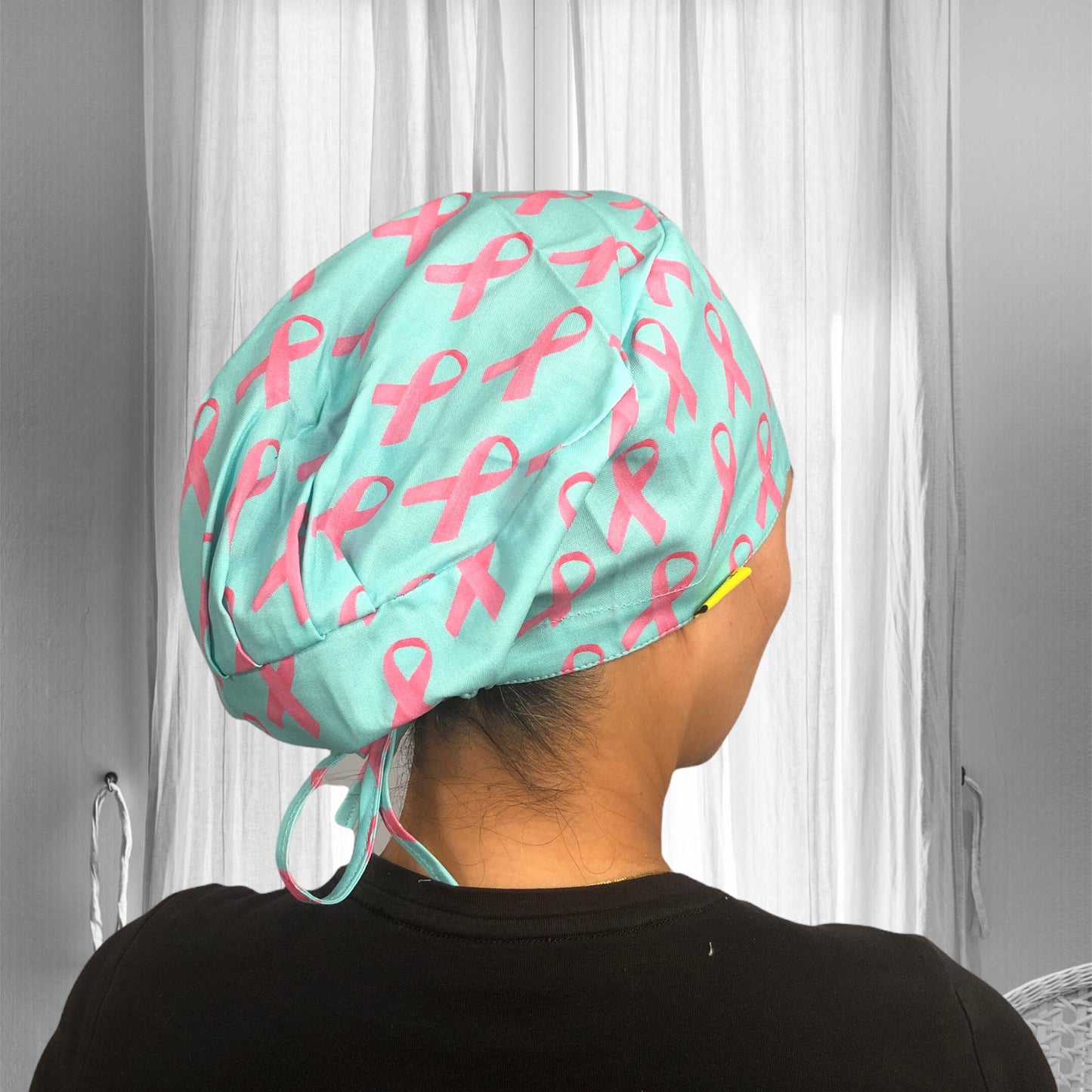 A light blue scrub cap featuring a pattern of pink ribbons, commonly associated with breast cancer awareness.