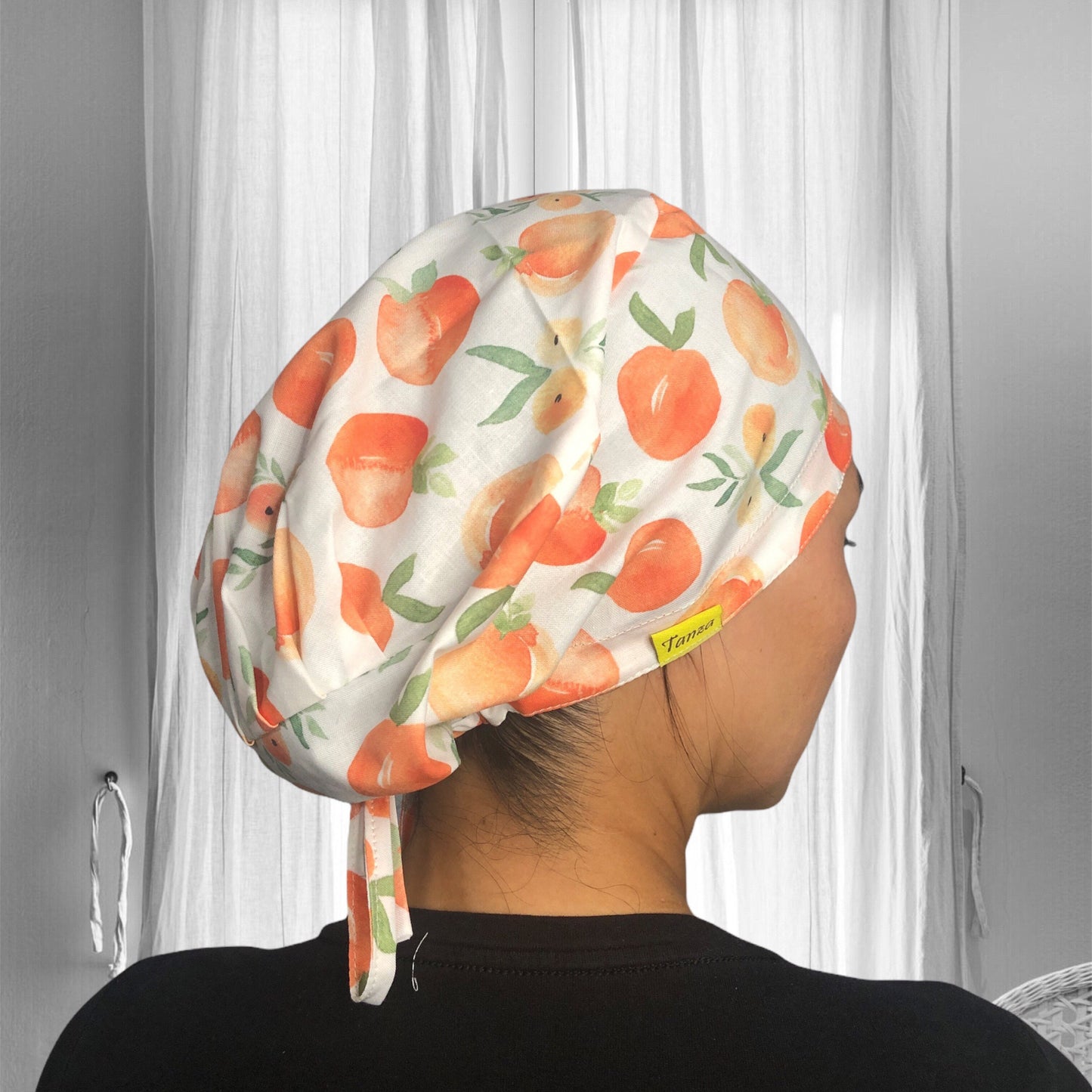 A person wearing a colorful scrub cap featuring a vibrant peach pattern with green leaves.