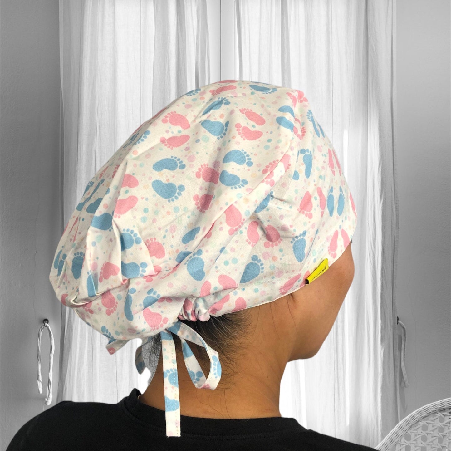 A colorful scrub cap featuring a playful pattern of blue and pink baby footprints.