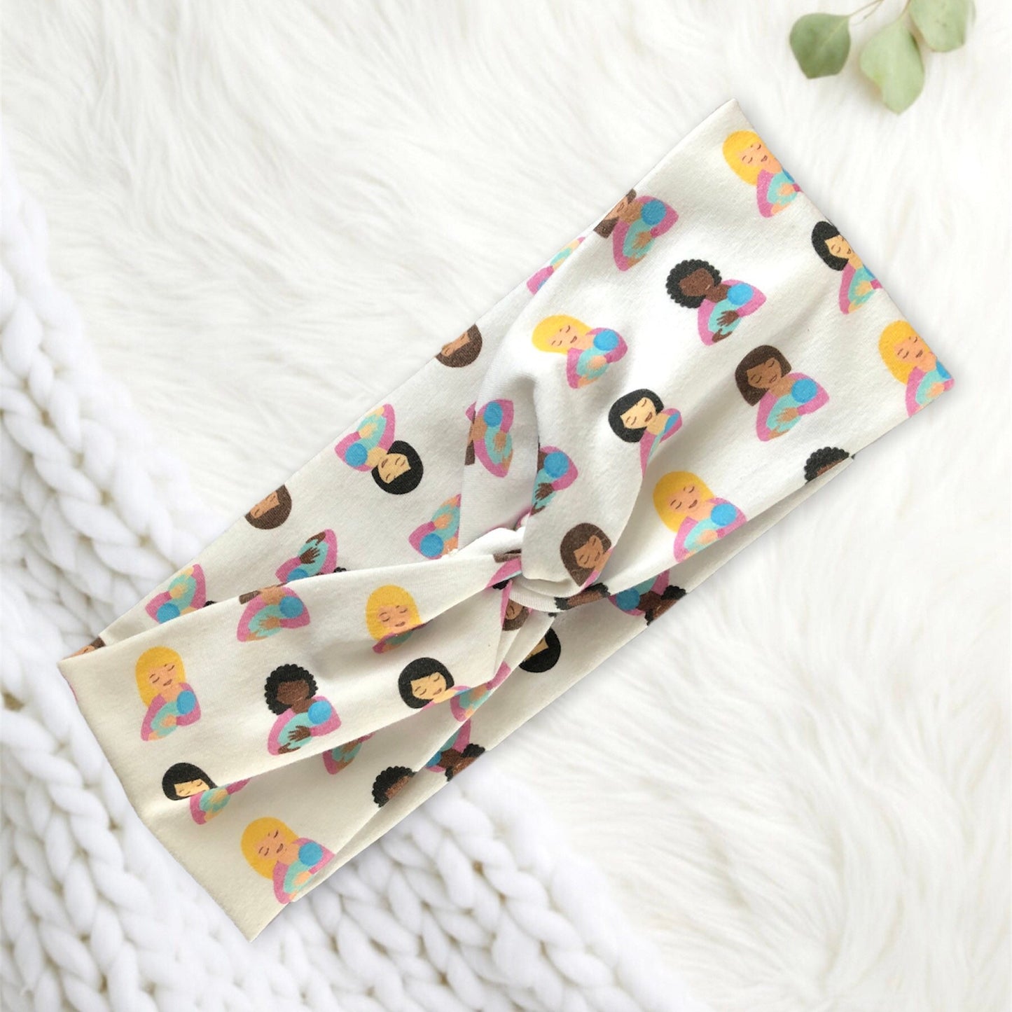A soft, patterned headband featuring diverse illustrations of women breastfeeding her baby against a white, textured background. The design includes various hair colors and skin tones, creating a vibrant and inclusive look.