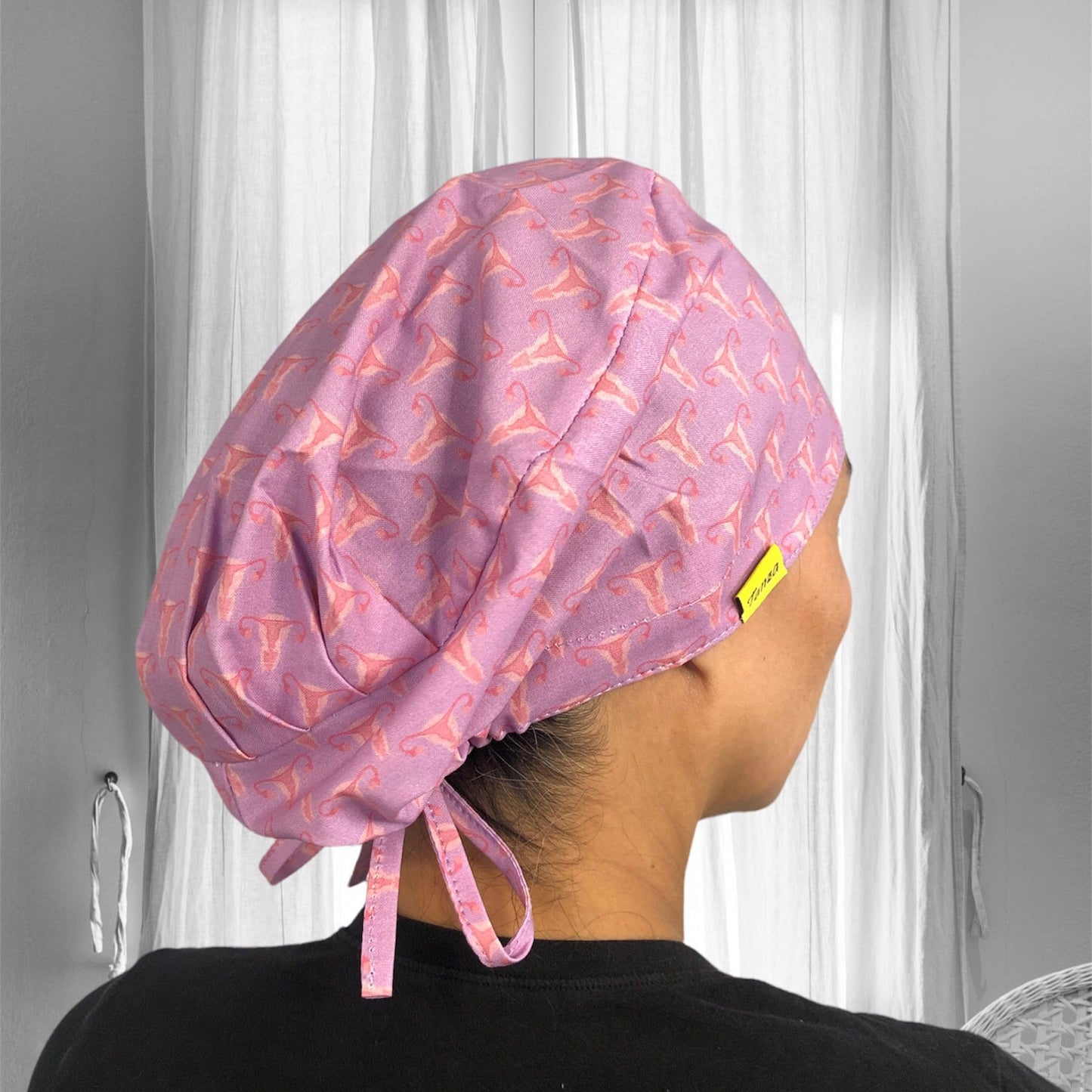 A person wearing a light purple scrub cap featuring a pink uterus pattern.