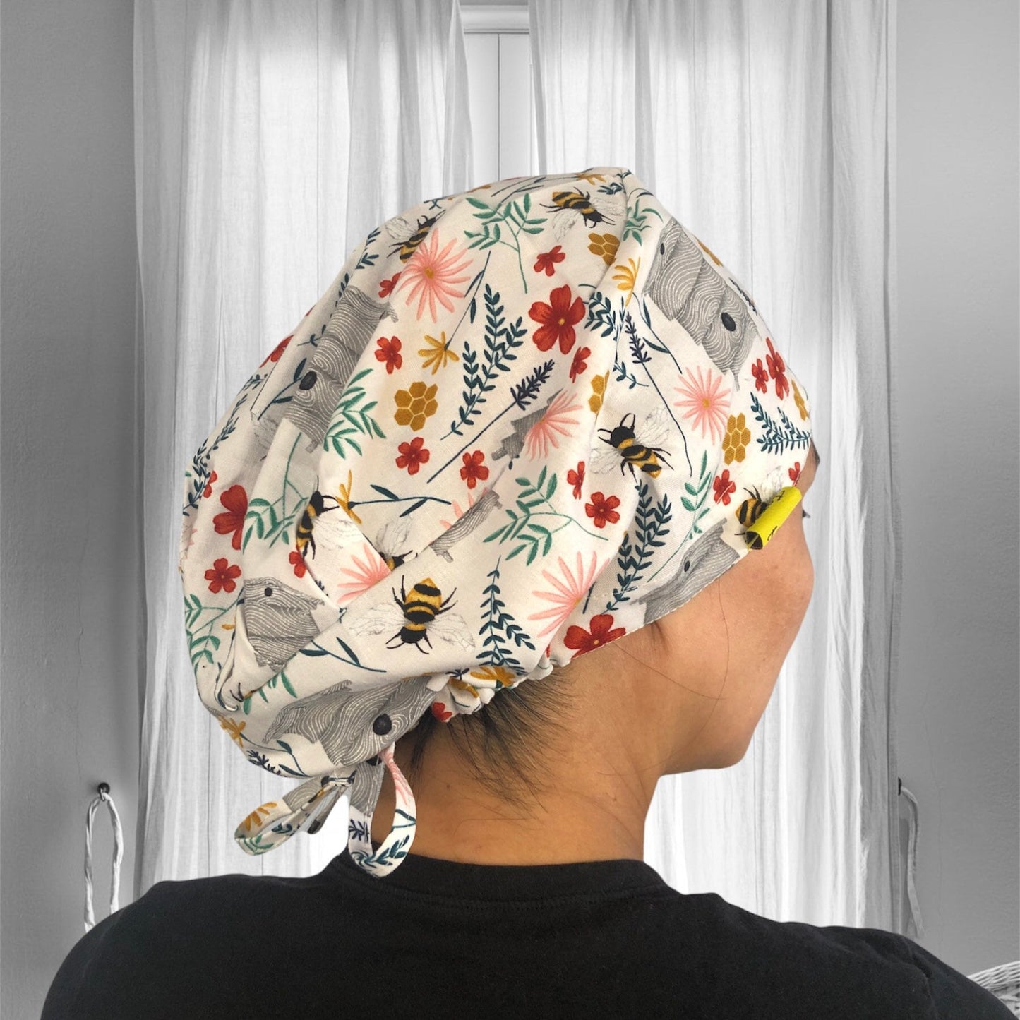 A person is wearing a patterned scrub cap with a variety of colorful floral designs, including bees and leaves.