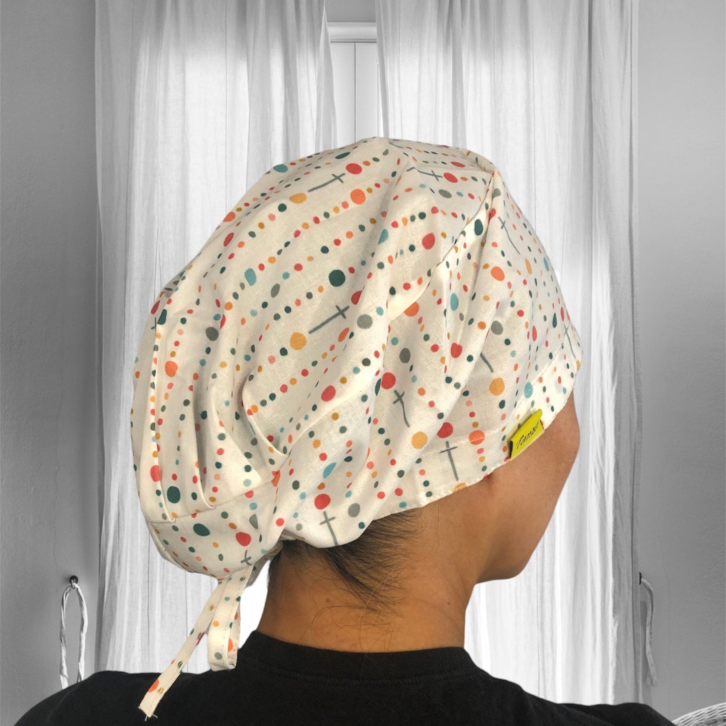 A person wearing a colorful scrub cap. The cap features a playful pattern of dots and crosses in various colors such as orange, yellow, teal, and red, against a white fabric background.