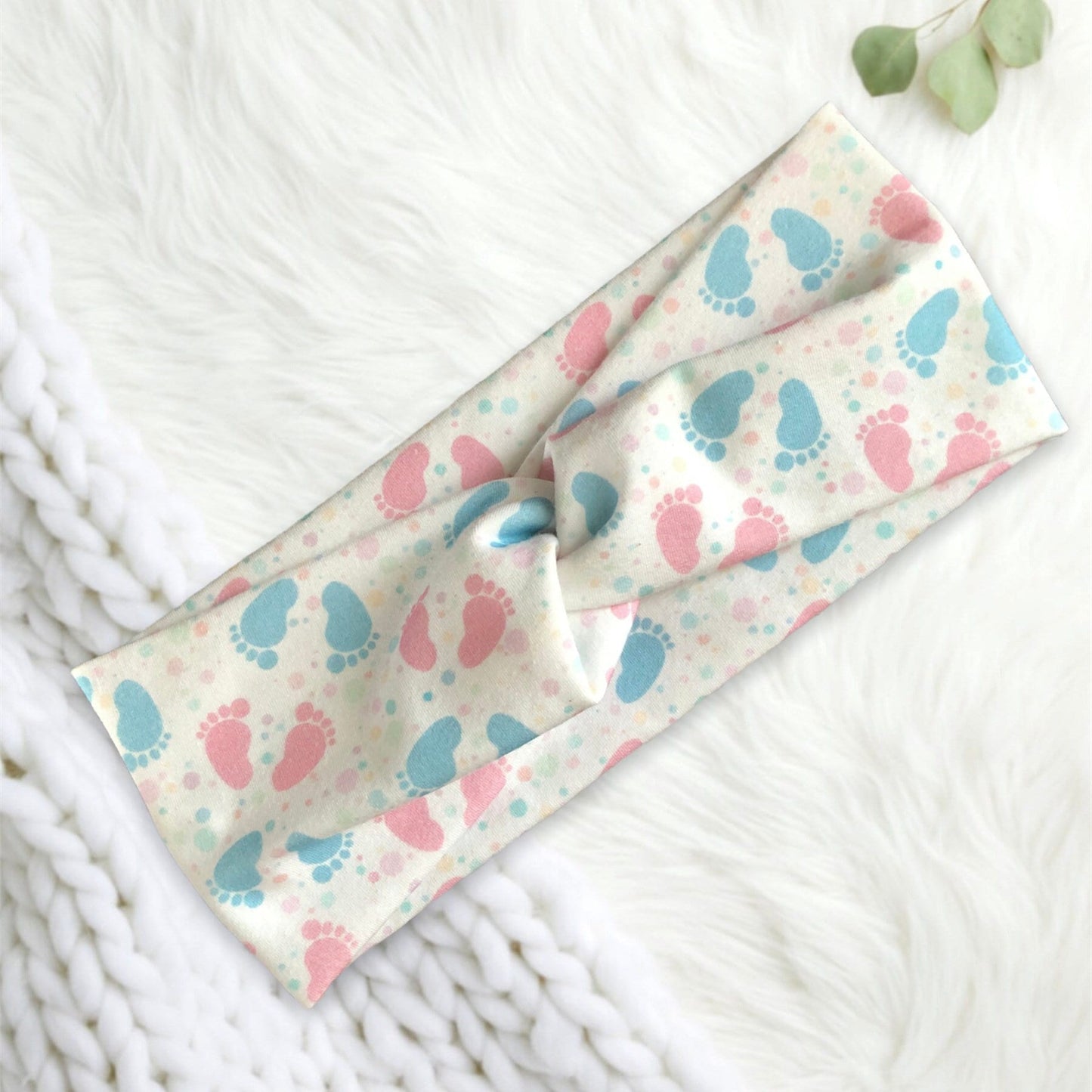 A soft, fabric headband featuring a playful pattern of pink and blue baby footprints.