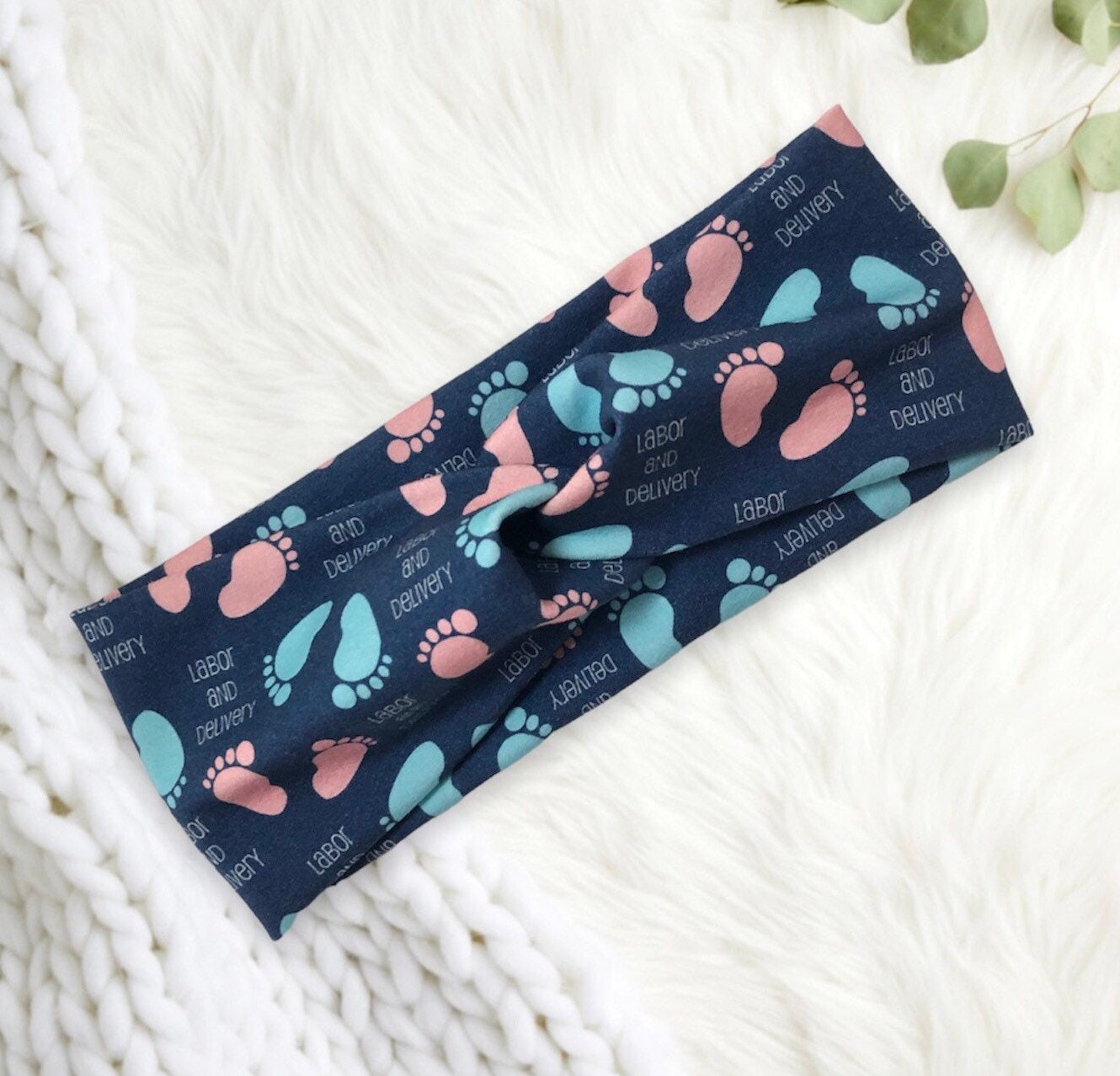 The headband is patterned with baby footprints in pink and blue, along with the words "labor and delivery" in white.