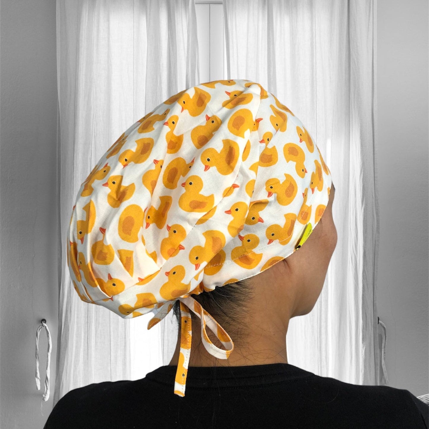 A soft, scrub cap adorned with a playful pattern of yellow rubber ducks on a white background.