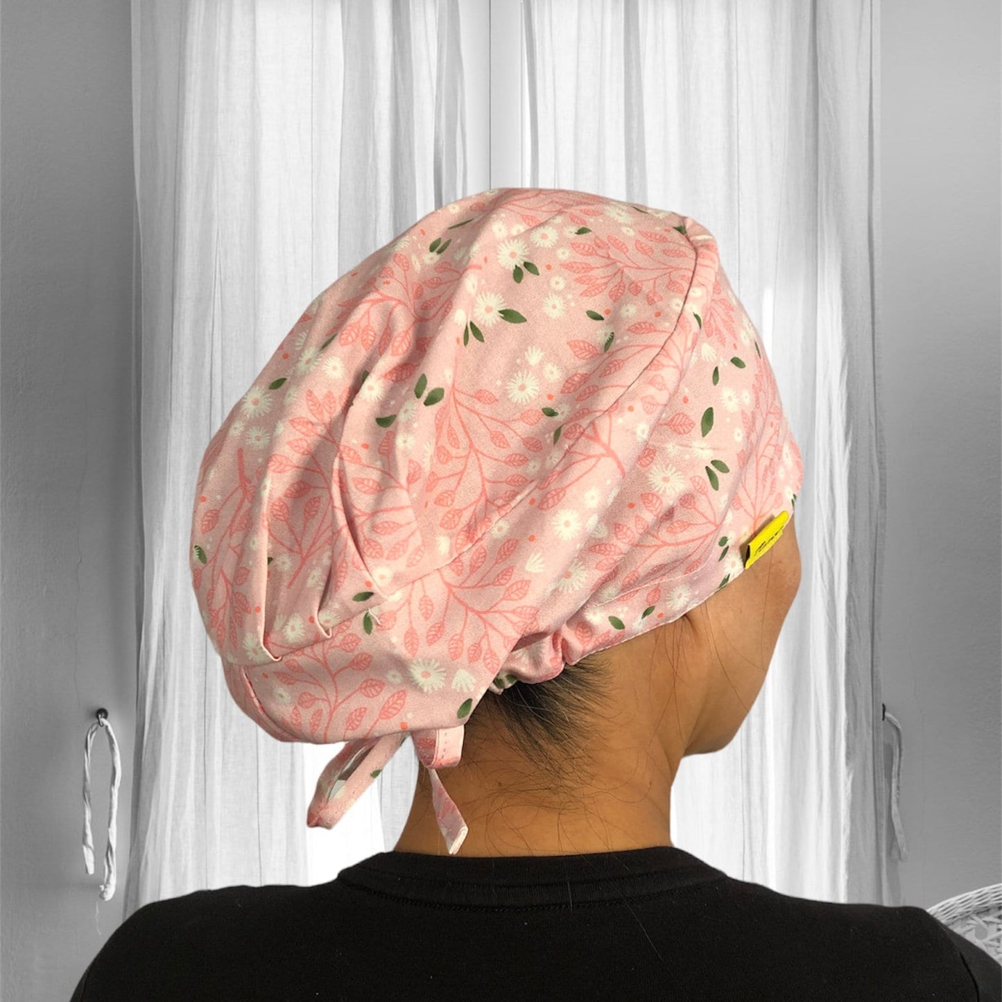 A pink floral-patterned scrub cap, with leaf and flower designs. The fabric appears soft and the cap is tied at the back, suggesting an adjustable fit.