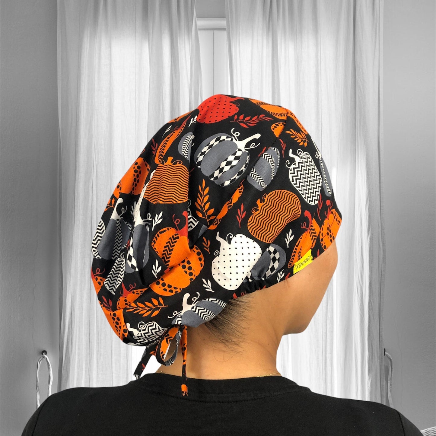A vibrant and stylish scrub cap featuring a playful design of pumpkins in various patterns and colors like orange, black, and white.
