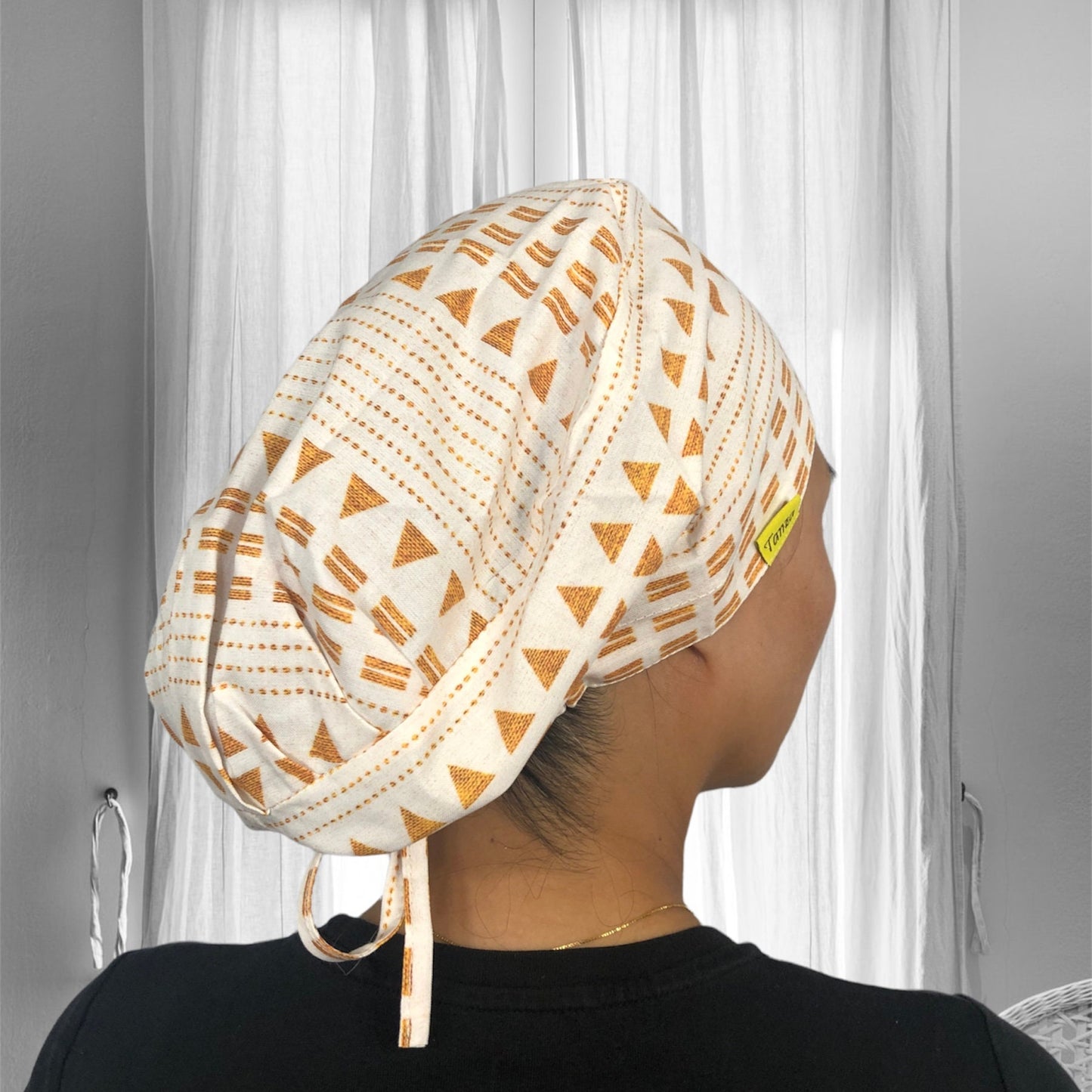 A stylish scrub cap with a geometric pattern. The design features orange triangles and dotted lines on a cream fabric background.