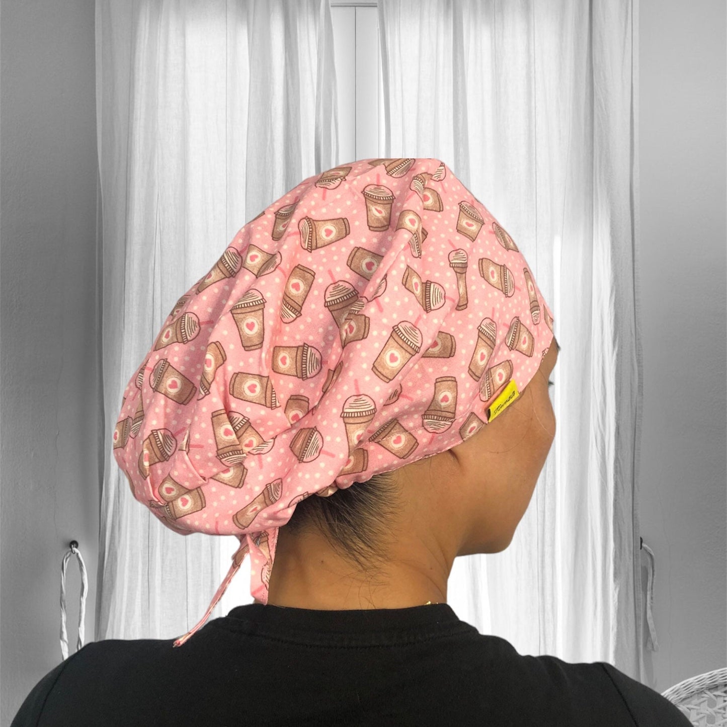 A person wearing a pink scrub cap adorned with playful coffee cup patterns.