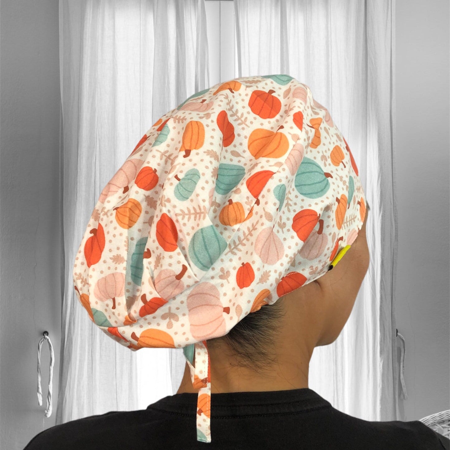 A person wearing a colorful scrub cap with a pattern of pumpkins and leaves in shades of orange, teal, and beige.