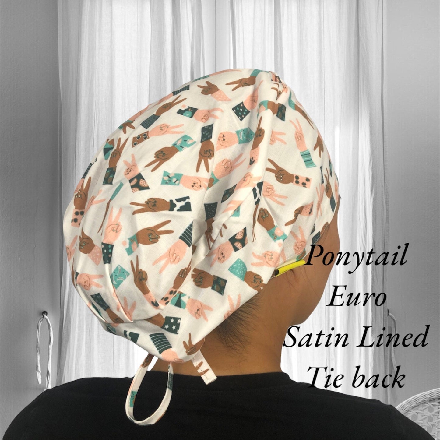 A soft, knotted scrub cap with a playful pattern featuring cartoon peace signs in various pastel outfits.