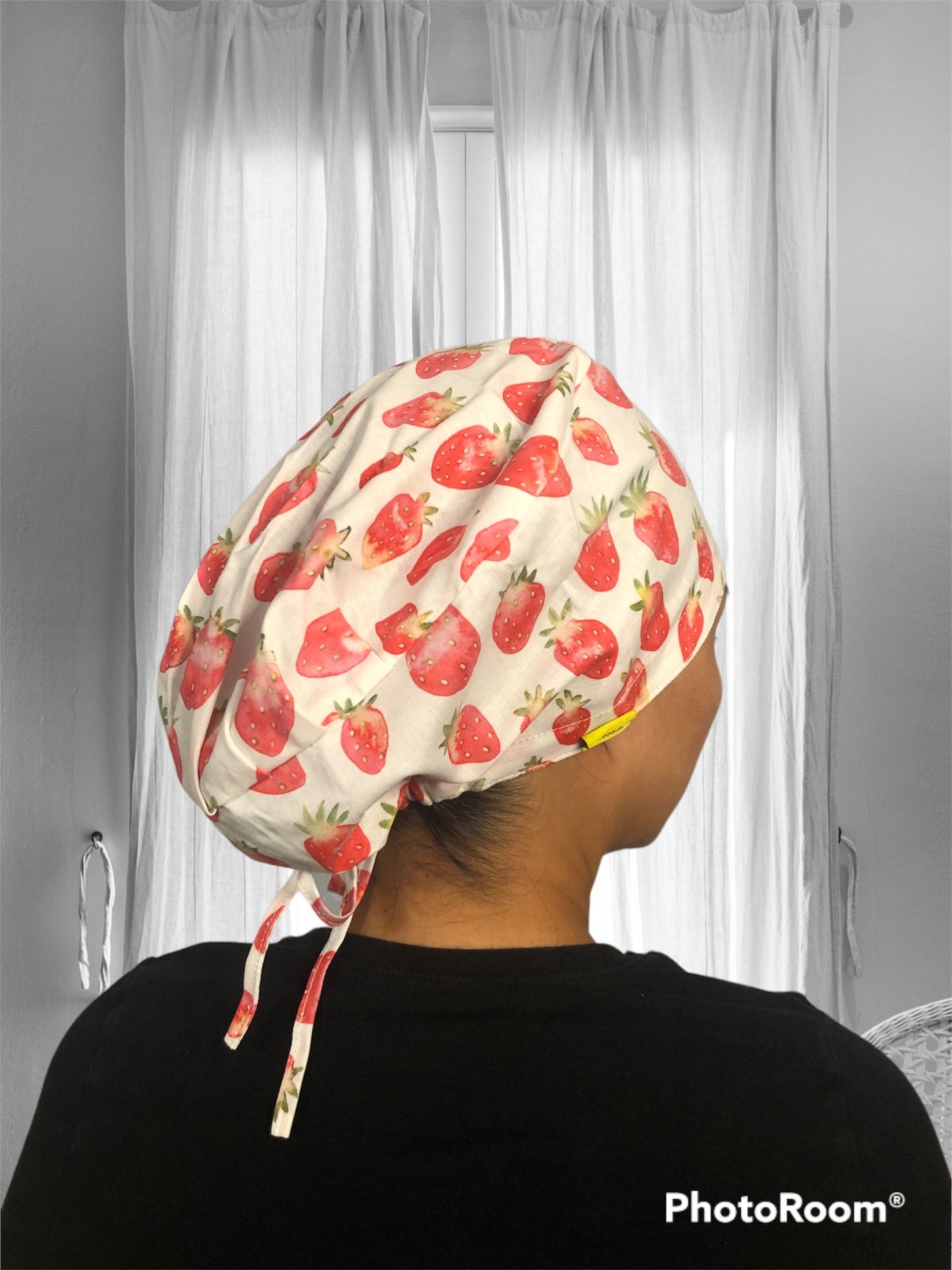 A person wearing a scrub cap with a vibrant strawberry pattern. The cap features various shades of red strawberries scattered across a light-colored fabric.