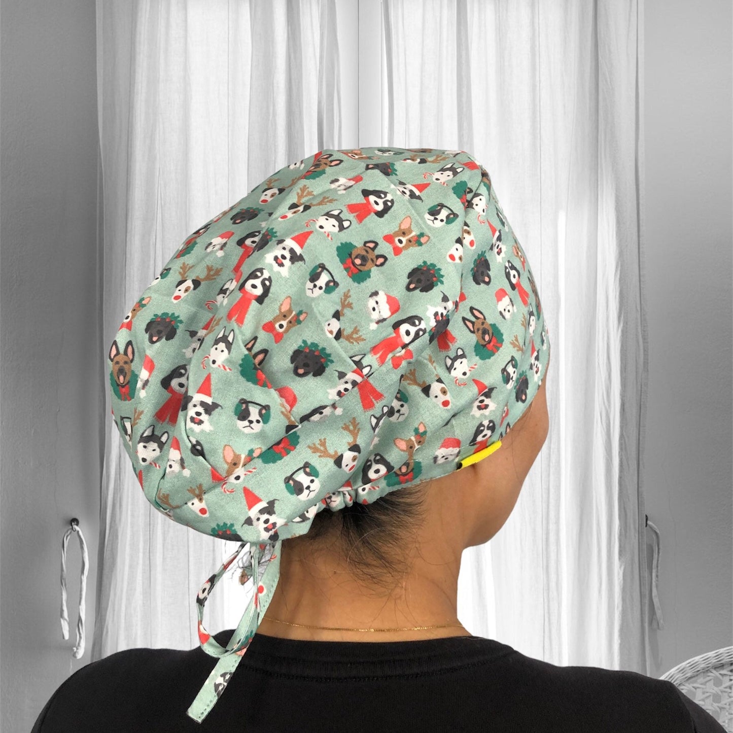 A scrub cap with a playful design featuring various dog faces and holiday-themed elements like Santa hats and reindeer antlers, set against a light green background.