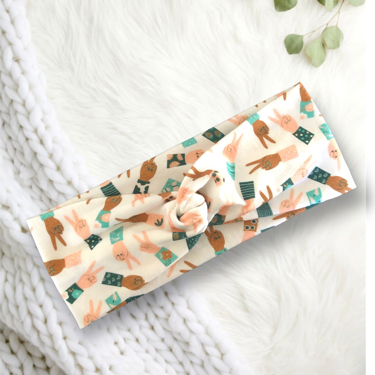 A soft, knotted headband with a playful pattern featuring cartoon peace signs in various pastel outfits.