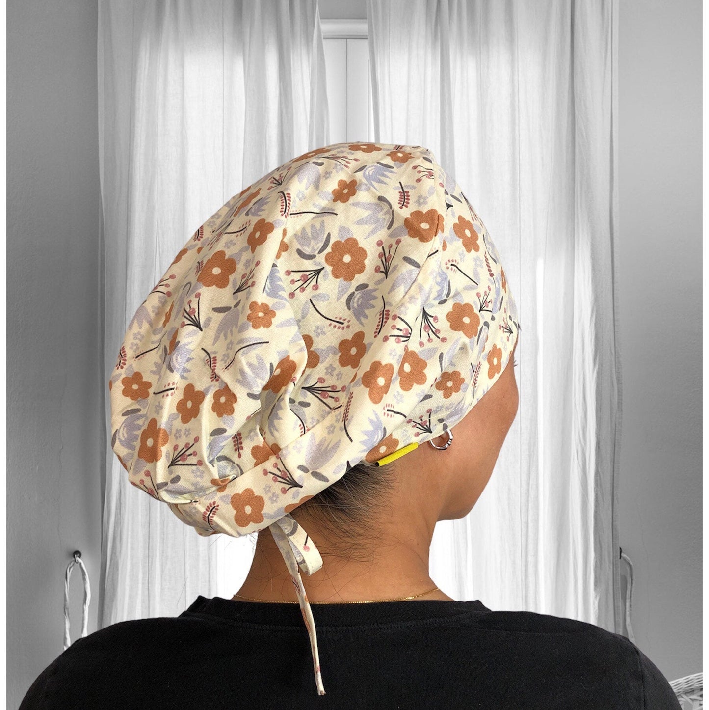 A person wearing a light-colored scrub cap with a floral print design featuring orange and pastel flowers.