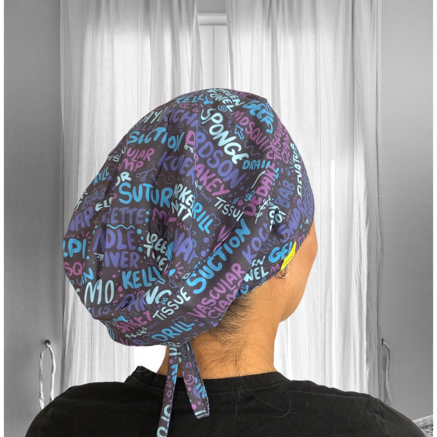A colourful scrub cap with a variety of medical terms and phrases printed all over in vibrant shades of blue, pink, and purple.