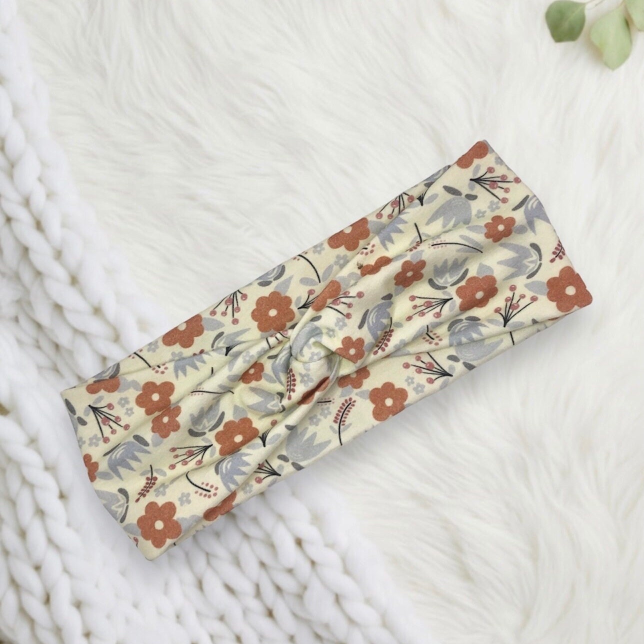 A light-colored headband with a floral print design featuring orange and pastel flowers.