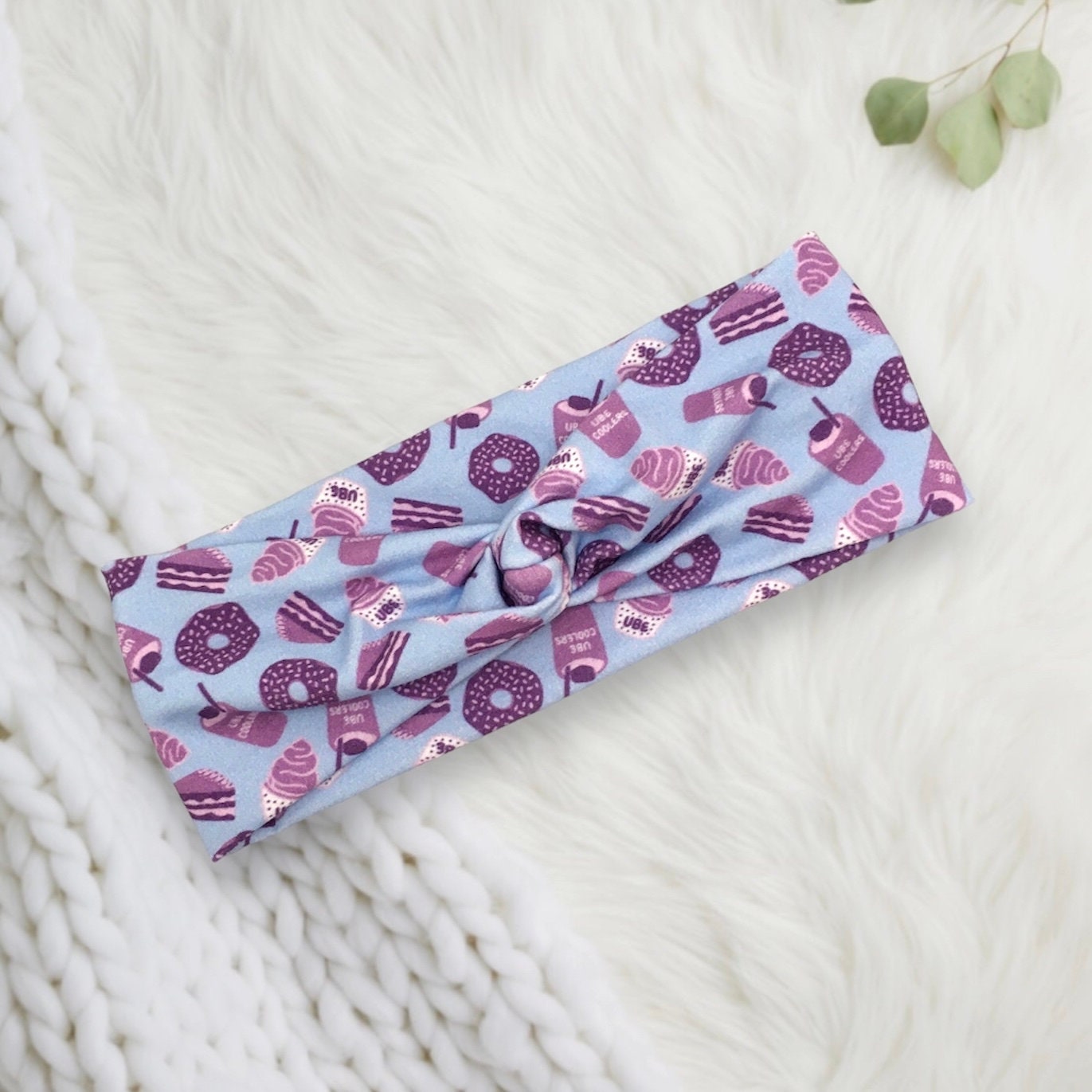 A pastel blue fabric headband featuring a playful pattern of purple and pink desserts, including donuts, cupcakes, and slices of cake.