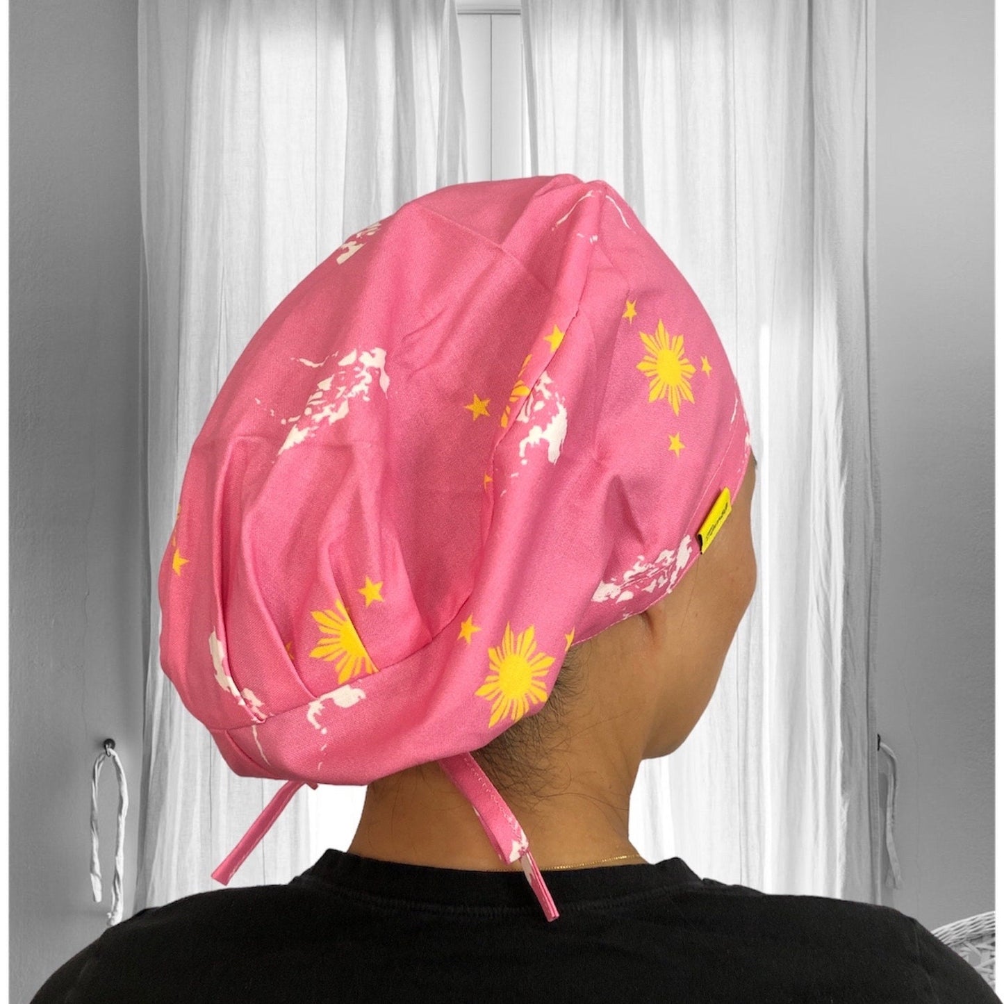 A person wearing a pink scrub cap with yellow sun and star designs, reminiscent of the Philippine flag's symbols.