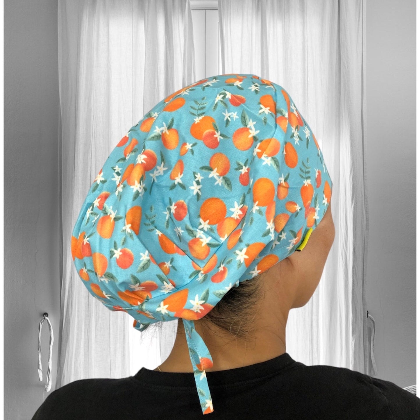 A person wearing a stylish scrub cap with a vibrant design of oranges and white flowers on a light blue background.
